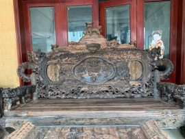 Đoản dài đục tay full họa tiết: đỉnh chương đục Nghê vờn cầu, tay cột Rồng khuỳnh uốn lượn, tay vịn nguyên khối đục cả con Nghê ôm cầu. Vách tựa đục Tam Long tranh châu. Toàn cảnh bức chương là một thế giới sinh động và oai hùng