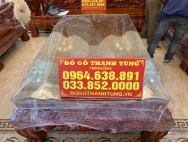 Chiếc bàn to mặt chạm Tứ Linh quần tụ, trên mặt phủ lớp kính trong dày bảo vệ mặt gỗ